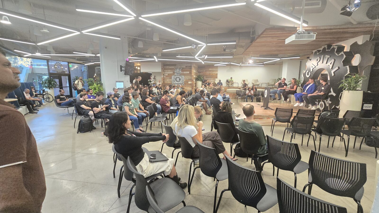 The full room seen from the side, audience in rows under the Capital Factory gear